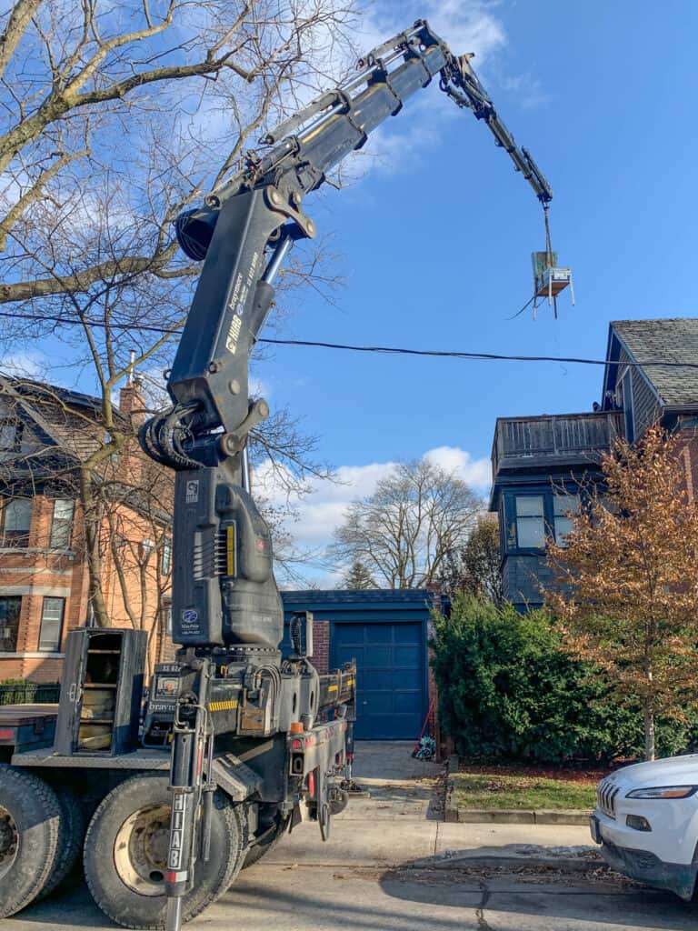 Using a knuckle crane to lift a juke box to a third floor balcony of a house