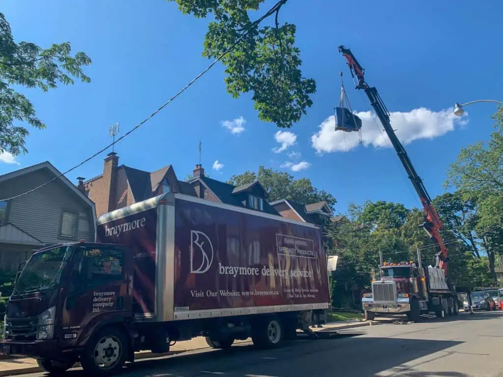 Using a crane to lift a grand piano over a house and land it on a backyard balcony