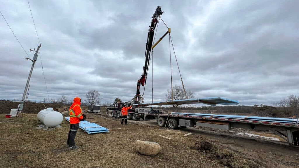 Crane lifting steel siding off a transport truck at a construction site