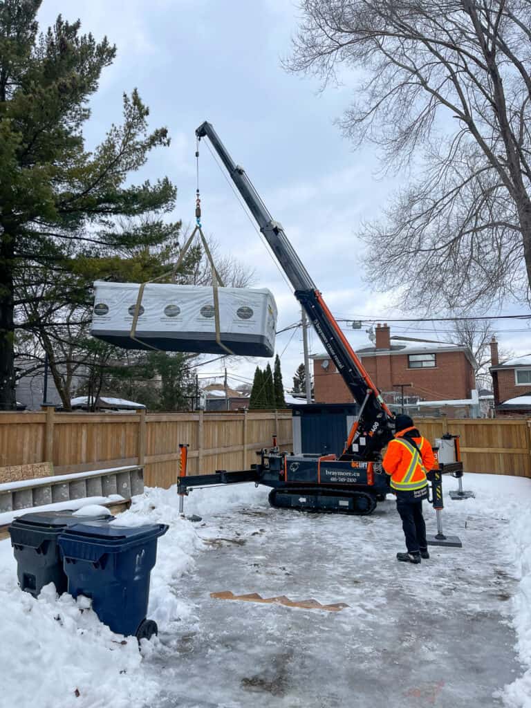 Spider crane lifting a swim spa over a fence from a neighbours backyard.