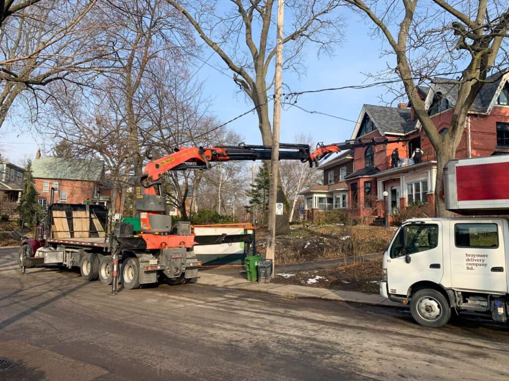 Crane under a power line to avoid some trees lift furniture to a second floor of a house. 