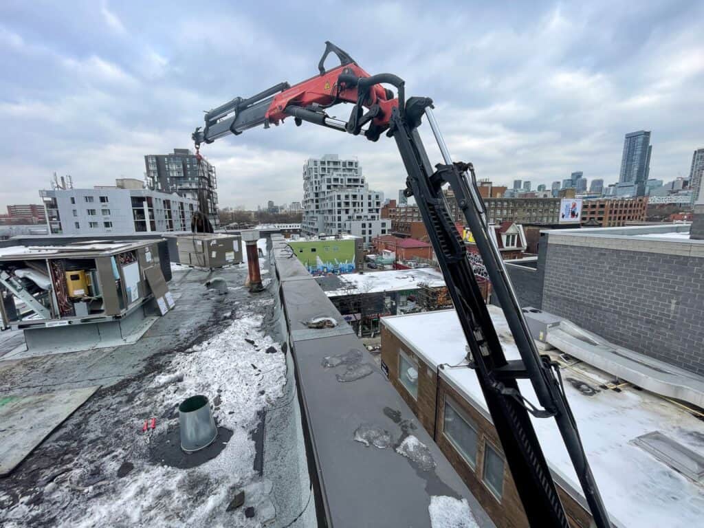 Knuckle crane lifting an HVAC up onto a commercial building from a very tight laneway.