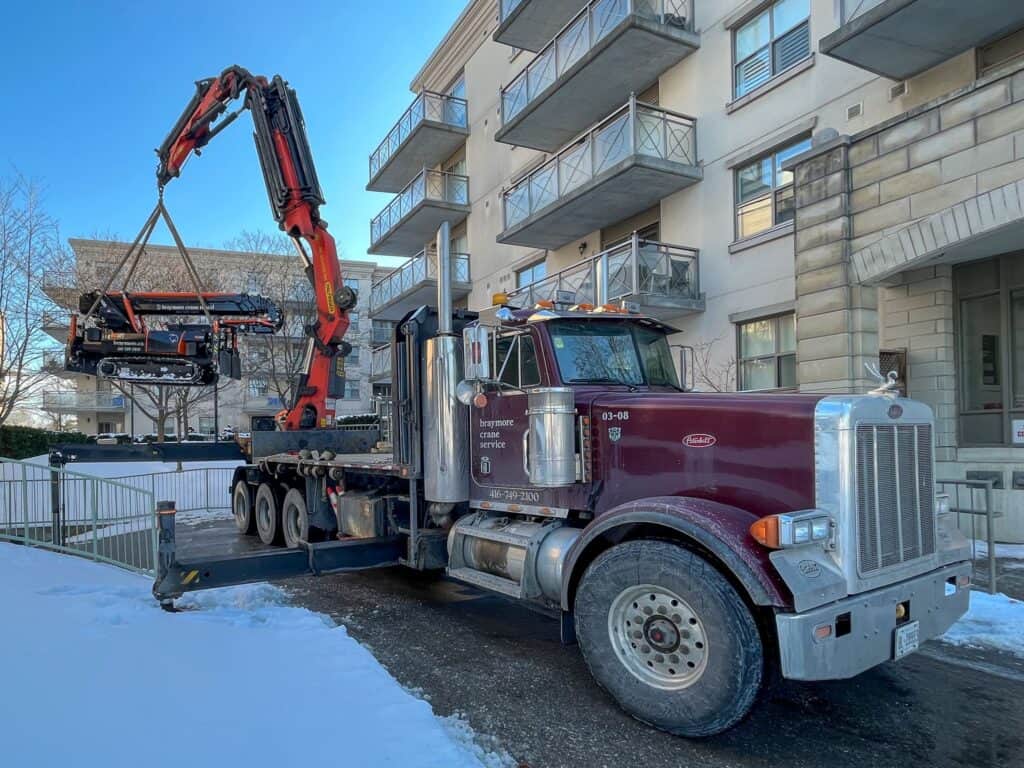 A Knuckle crane lifting a spider crane over a fence to do a lift at an apartment complex