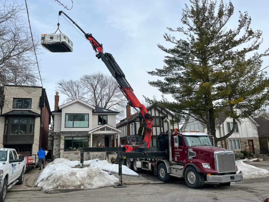 Using a knuckle crane to lift a hot tub over a house that will not fit between the houses