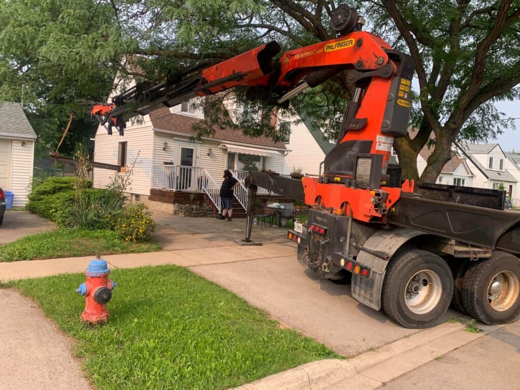 Reaching under a tree with a knuckle crane to get a large heavy steel beam into a home.