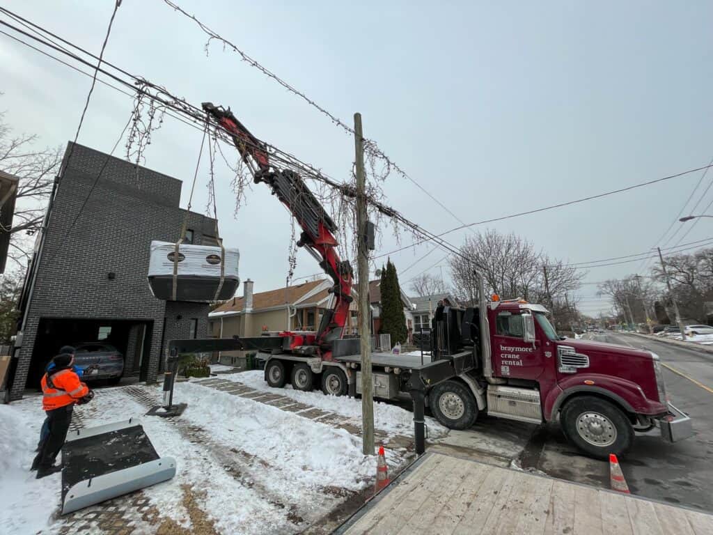 Using a knuckle crane to lift a hot tub over a house that will not fit between the houses