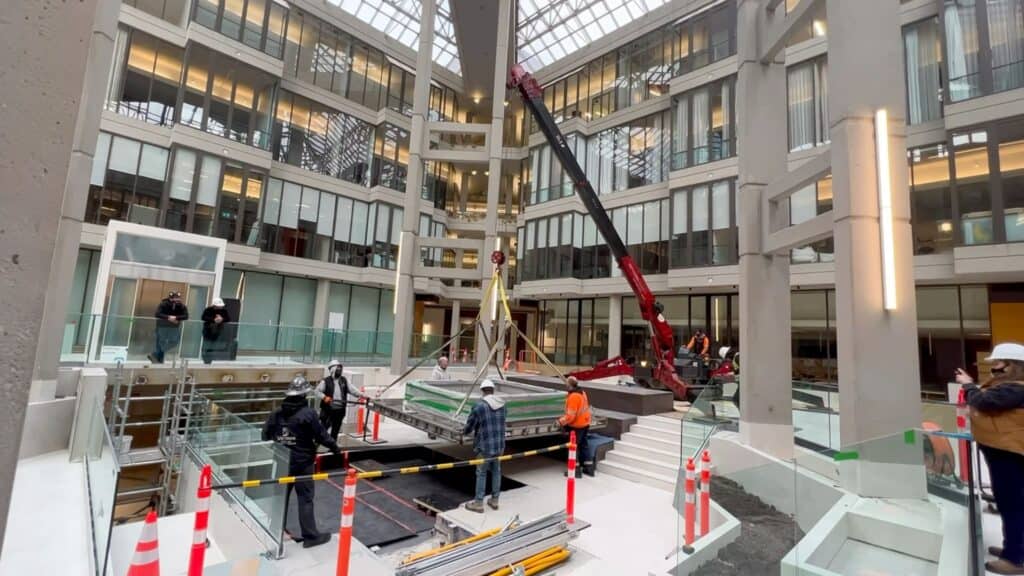 A spider crane lifting indoors a water feature in a building lobby.