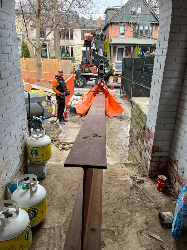 Knuckle crane lifting a steel beam to the front entrance of a home in Toronto